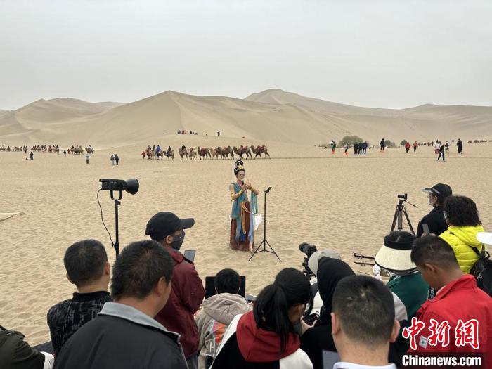 圖為2023年4月底，敦煌大漠“逐舞者”奧楠在鳴沙山月牙泉景區(qū)視頻直播，吸引游人圍觀。　馮志軍 攝